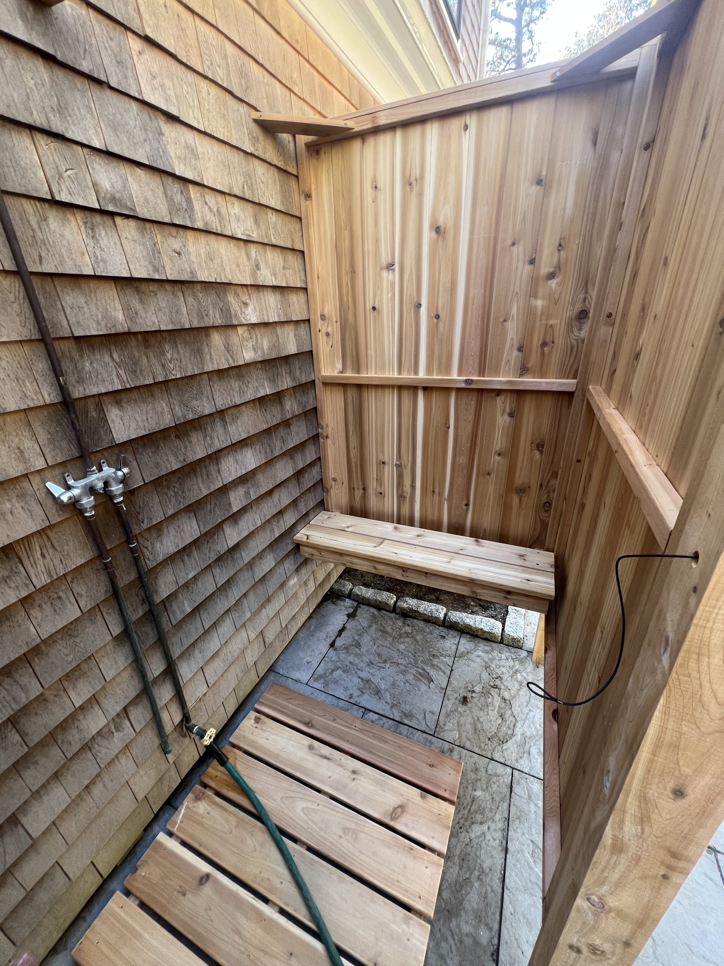 Cedar outdoor shower enclosure with stone floor and wood bench.